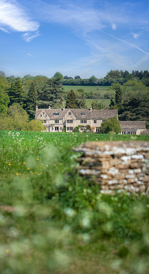 View across Cotswold farmland towards a large Cotswold stone manor house nestled in the beautiful landscape.