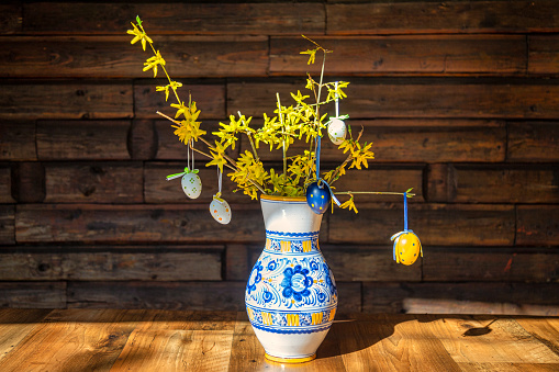 Still life with easter decoration, ceramic vase with easter eggs on twigs of forsythia.