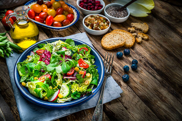 Healthy eating: high angle view of a fresh salad plate shot on rustic wooden table. Some ingredients for preparing salad like avocado, tomatoes, berries, chia seeds, asparagus, green beans, mixed nuts, broccoli, and olive oil are all around the plate. Useful copy space available for text and/or logo. High resolution 42Mp studio digital capture taken with SONY A7rII and Zeiss Batis 40mm F2.0 CF lens