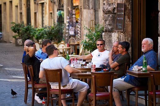 Local men sitting outside a cafe terrace in the afternoon with coffee and soft drinks in the city center of Rome, Italy.