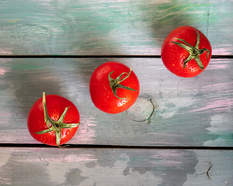 Three red tomatoes with leaves lie on a wooden turquoise table diagonally, shot from a top viewpoint