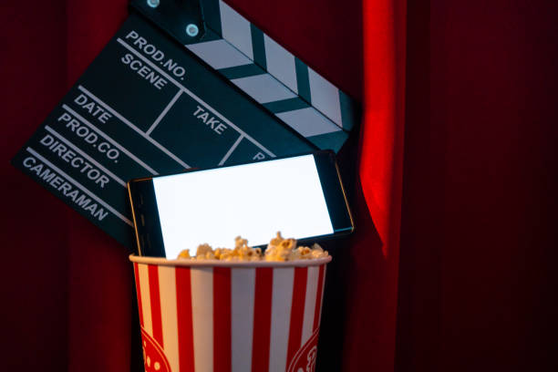 istock mobile phone with empty white bright screen with popcorn bucket and movie clapper board. Concept of streaming TV on internet phone. 1221814540