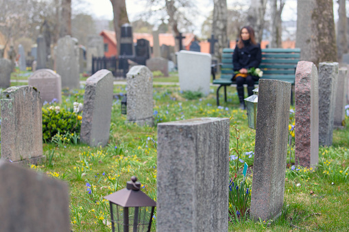 A woman sitting alone at a bench in the cemetery.