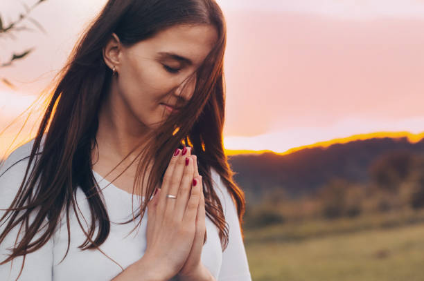 ritratto di una donna single che prega e guarda verso il tramonto. mani piegate nel concetto di preghiera per la fede, la spiritualità e la religione. - spirit medium foto e immagini stock