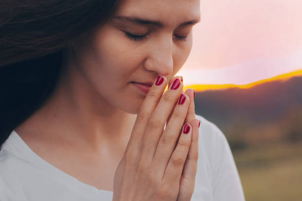 ritratto di una donna single che prega e guarda verso il tramonto. mani piegate nel concetto di preghiera per la fede, la spiritualità e la religione. - spirit medium foto e immagini stock