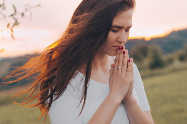 ritratto di una donna single che prega e guarda verso il tramonto. mani piegate nel concetto di preghiera per la fede, la spiritualità e la religione. - spirit medium foto e immagini stock