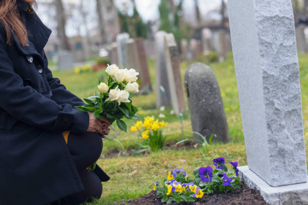 Woman visiting a grave with flowers A woman with flowers kneeling by a grave at the cemetery. death stock pictures, royalty-free photos & images