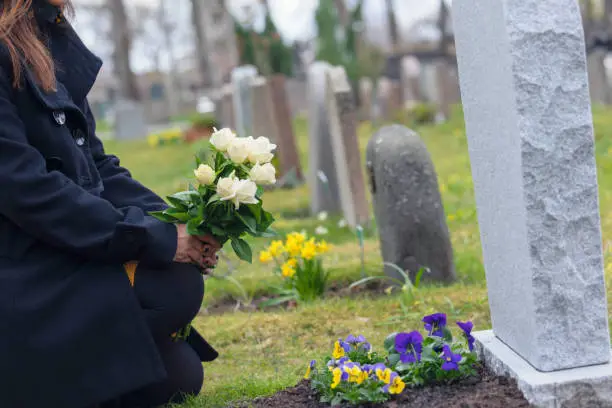 A woman with flowers kneeling by a grave at the cemetery.
