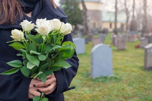 A woman holding a bouquet of white roses while visiting the graveyard.