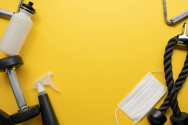 Gym equipment on yellow background with Mask and cleaning stuff