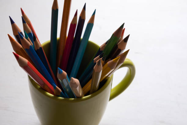 istock Multi-colored pencils in green cup on wooden white table background - front view 1221818936