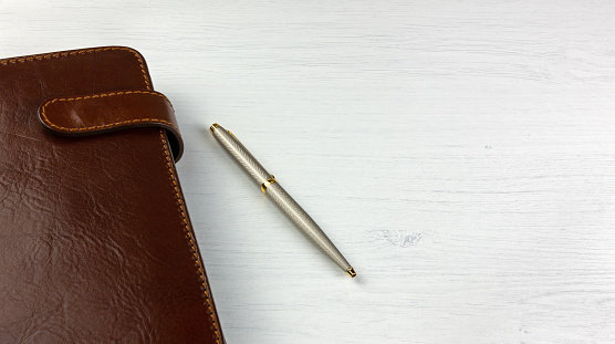 Elegant pen and daily planner with a leather cover on a white wooden desk