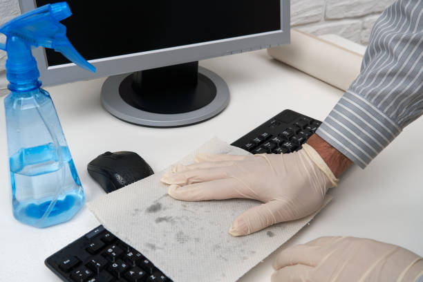 concept of cleaning or disinfecting the office - a businessman cleans the workplace, computer, desk, uses a spray gun and paper napkins. Cleaning surfaces from microbes, viruses and dirt. concepto de limpieza o desinfección de la oficina - un hombre de negocios limpia el lugar de trabajo, computadora, escritorio, utiliza una pistola de pulverización y servilletas de papel. limpieza de superficies de microbios, virus y suciedad.
