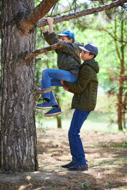 istock A boy helping to a girl climbing in a tree, bright sunlight, beautiful day 1221825914