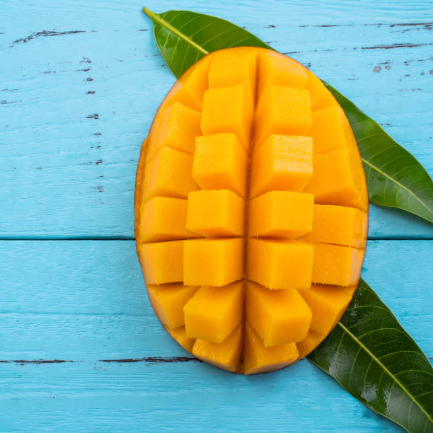 istock Mango - Fresh chopped tropical mango fruit isolated on bright vibrant light blue wooden table background, top view, flat lay layout, overhead shot. 1221826083