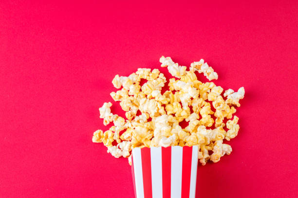 istock Paper cup with popcorn on color background. Striped box with popcorn on red background.Popcorn in red and white striped cardboard bucket . 1221826244
