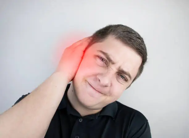 Photo of A man suffers from pain in the ear. The auditory meatus hurts due to otitis media, cerumen plug, ear boil, or trigeminal neuralgia