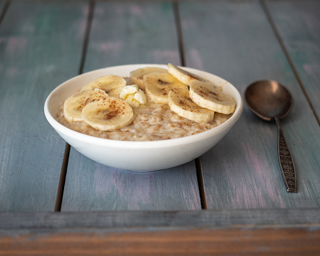 Milk oatmeal with banana and cinnamon in a deep plate and spoon on a wooden background. View from above