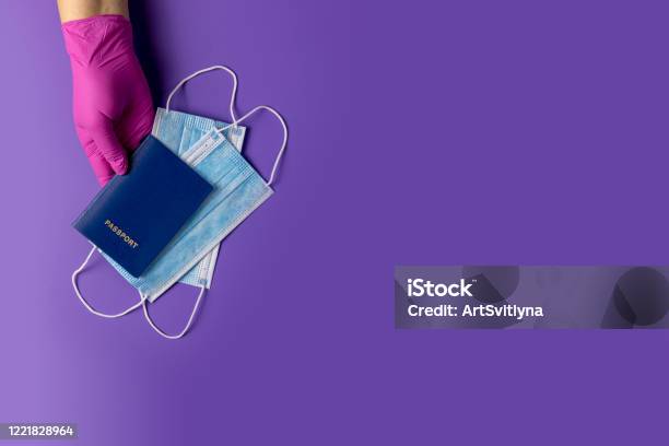 Doctor Holds Passports And Respiratory Surgical Face Mask In Hands Pink Medical Glove On Violet Background Stock Photo - Download Image Now