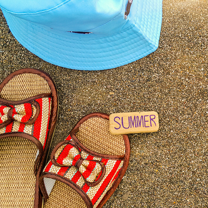 Part of the straw beach sandals and part of the hat on the sand by the sea. A small wooden sign with the inscription summer. Summer holidays. The beach background. Tourist holidays.