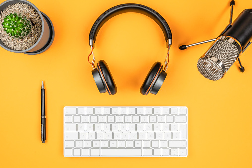 podcasting and podcast recording concept, top view of microphone, headphones and computer keyboard on orange desk