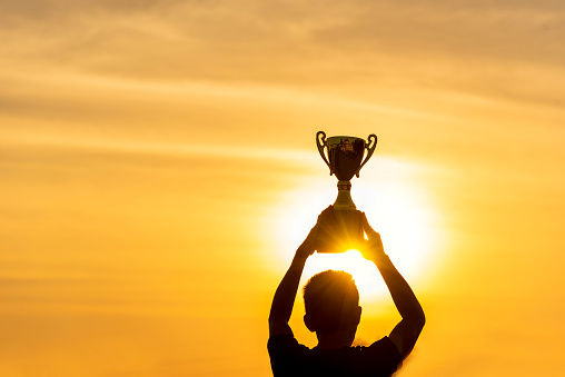 Winner win holding golden champion trophy cup prize. Silhouette best award victory trophy for professional champion challenge team holding gold sport trophy cup over head. Win-Win sport team concept