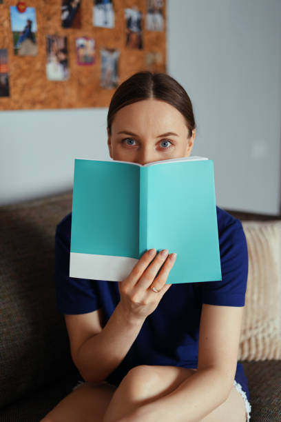 istock Attractive positive woman reading a book relaxing on the sofa 1221842806
