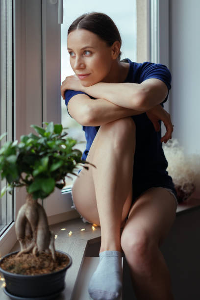 istock Young woman looking through window at the city 1221842816