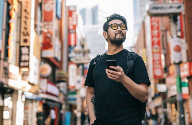 aziatische mens die de stad onderzoekt, die een smartphone in zijn hand houdt - reizen in azië stockfoto's en -beelden