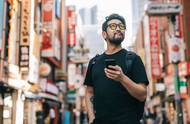 Photo of Asian Man Exploring The City, Holding a Smartphone in his Hand