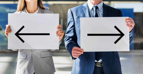 istock Business people standing while holding white Left and Right arrow placard in arrival area at airport 1221846041