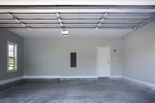 Empty large two-car garage with cement floors and a door to the inside as well as a garage door opener painted in a neutral gray color