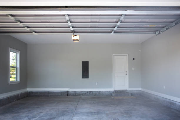 Empty large two-car garage with cement floors and a door to the inside as well as a garage door opener painted in a neutral gray color Empty large two-car garage with cement floors and a door to the inside as well as a garage door opener painted in a neutral gray color garage door opener photos stock pictures, royalty-free photos & images