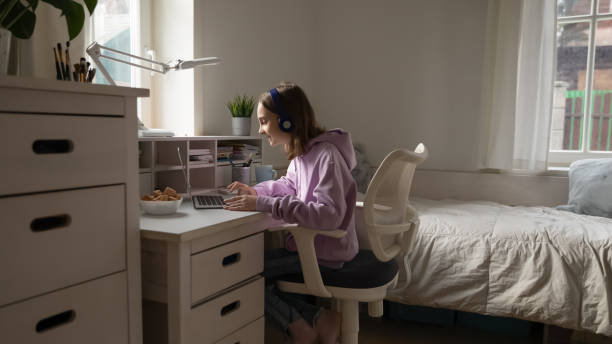 Teenage girl wearing headphones elearning from home using computer app