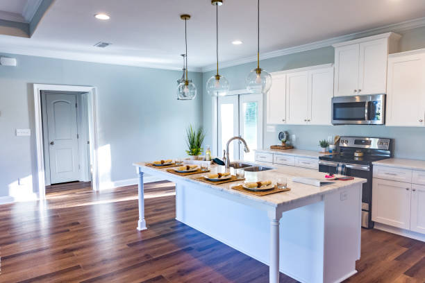 istock Open floor plan kitchen in a new construction empty house that has just been completed with white cabinets, pendant lighting, a bar area and hardwood floors 1221847433