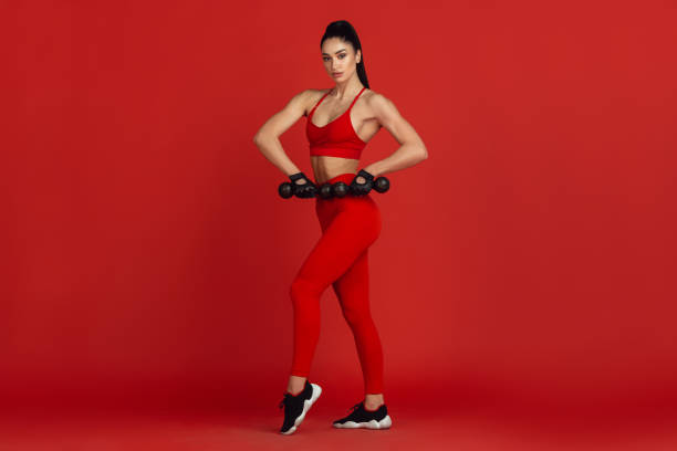 istock Beautiful young female athlete practicing on red studio background, monochrome portrait 1221848790