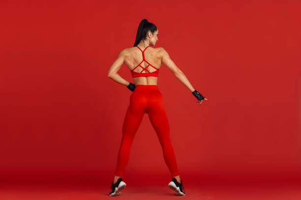 istock Beautiful young female athlete practicing on red studio background, monochrome portrait 1221848791