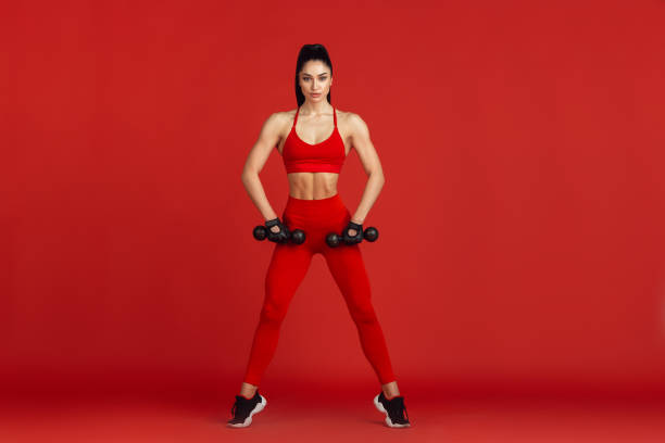 istock Beautiful young female athlete practicing on red studio background, monochrome portrait 1221848794