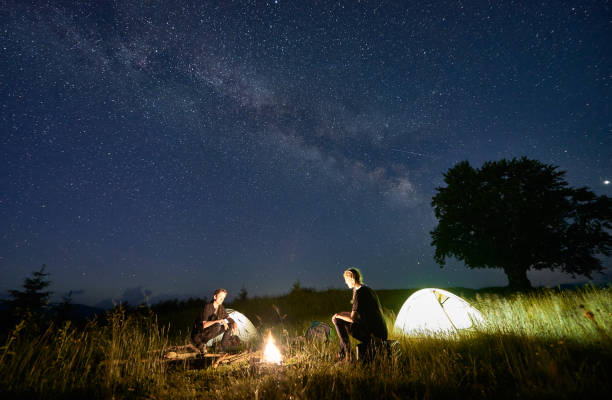 istock Friends travellers spending time in the mountains sitting around bonfire in camping under beautiful starry sky 1221852096