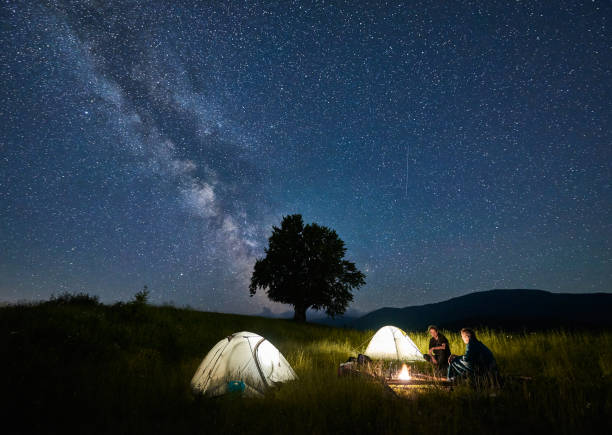 voyageurs d’amis passant le temps dans les montagnes s’asseyant autour du feu de joie dans le camping sous le ciel étoilé magnifique - camping family tent couple photos et images de collection