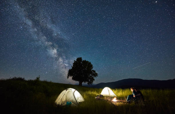 istock Young couple sitting near campfire under beautiful night sky. 1221852141