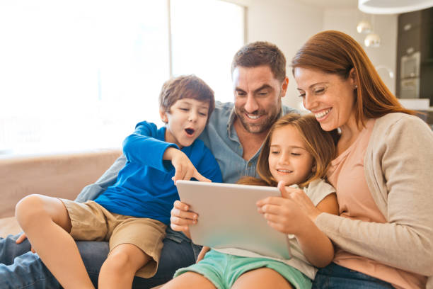 Family watching laptop during lockdown due to COVID-19 Parents and children sitting together on sofa in the living room and watching digital tablet. Family having video conference, staying at home due to pandemic COVID-19. argentinian ethnicity photos stock pictures, royalty-free photos & images