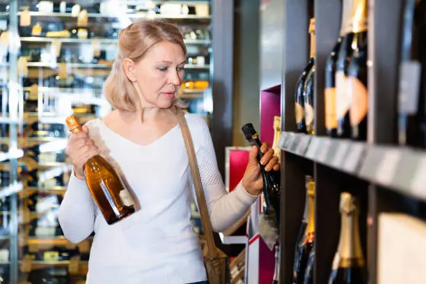 Portrait of happy  positive mature woman visiting winehouse in search of bottle of good wine