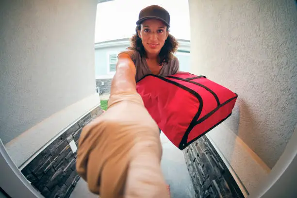 A young woman delivering takeout food to a home in the evening.
