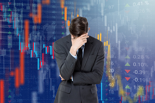 Worried businessman with head in hands in front of stock market data virtual interface