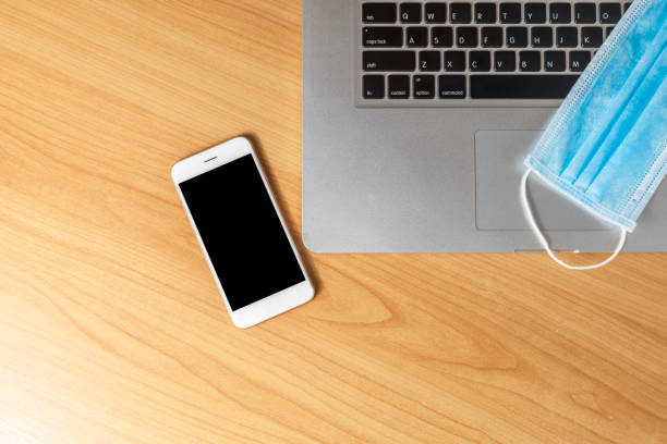 istock Work from home concept. Top view laptop, smartphone, and face mask on wood table with copyspace for text or design. 1221859772