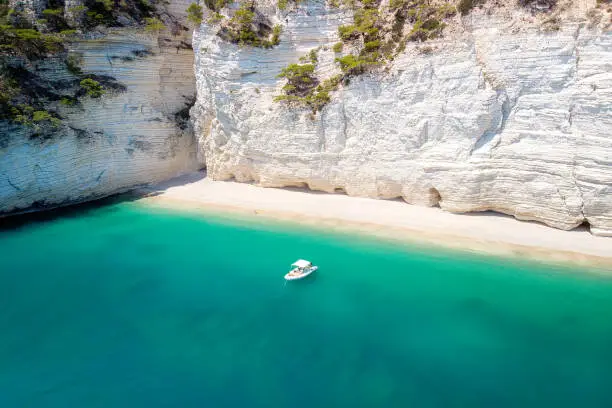 Recreation small boat in beautiful gulf with turquoise water. Faraglioni (sea stacks) in Puglia, Baia delle Zagare. Natural park Gargano with beautiful turquoise sea