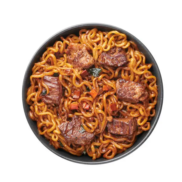 Photo of Ram-Don or Chapaguri noodles with beef steak in black bowl isolated on white background. Jjapaguri is a popular south korean dish with ramen and udon noodles and beef steak.