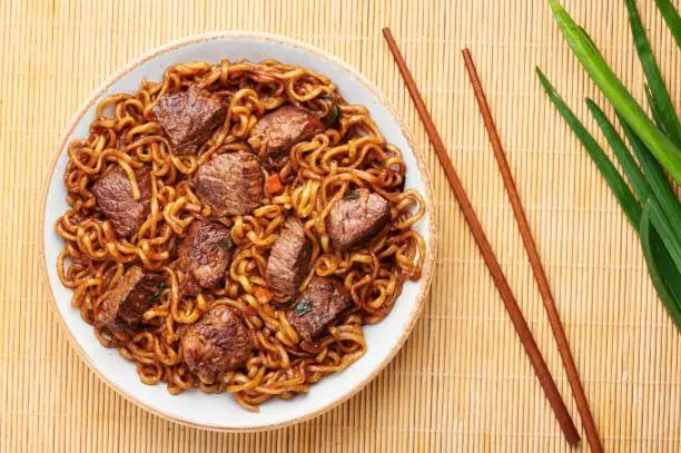 Photo of Ram-Don or Chapaguri noodles with beef steak in white bowl. Jjapaguri is a popular south korean dish with ramen and udon noodles and beef steak. Copy Space