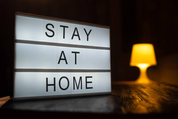 istock A sign with the text stay at home, a person working at a computer in a light on the background. COVID-19 Coronavirus STAY HOME SAVE LIVES viral social media message sign with text for social 1221862231